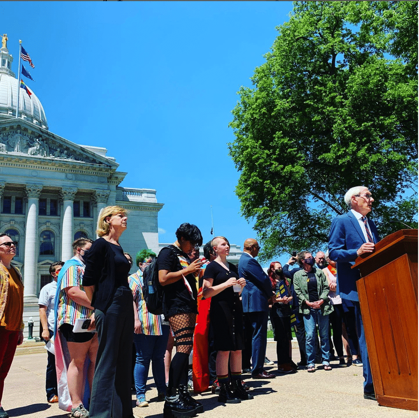 Fair Wisconsin Staff and community members standing behind Governor Tony Evers as he raises the pride flag