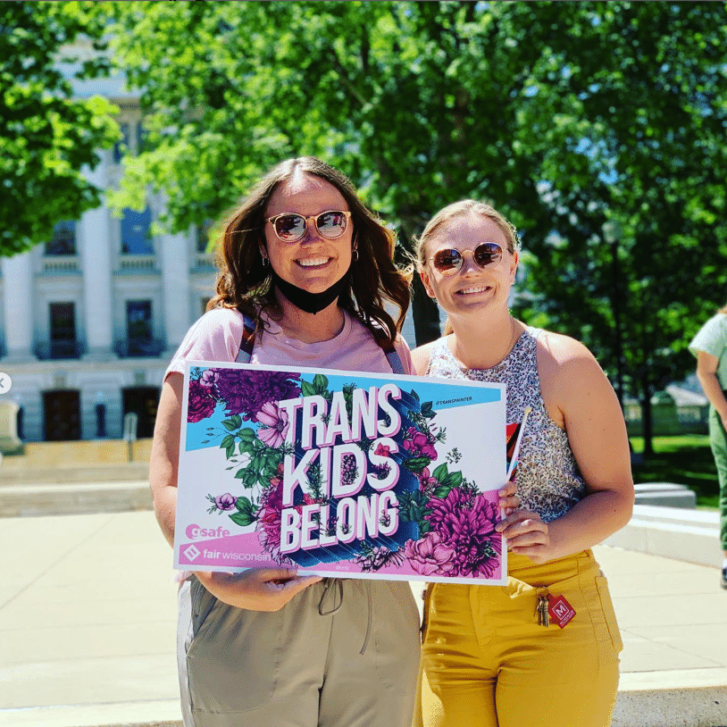 Two people holding a sign that says Trans Kids Belong